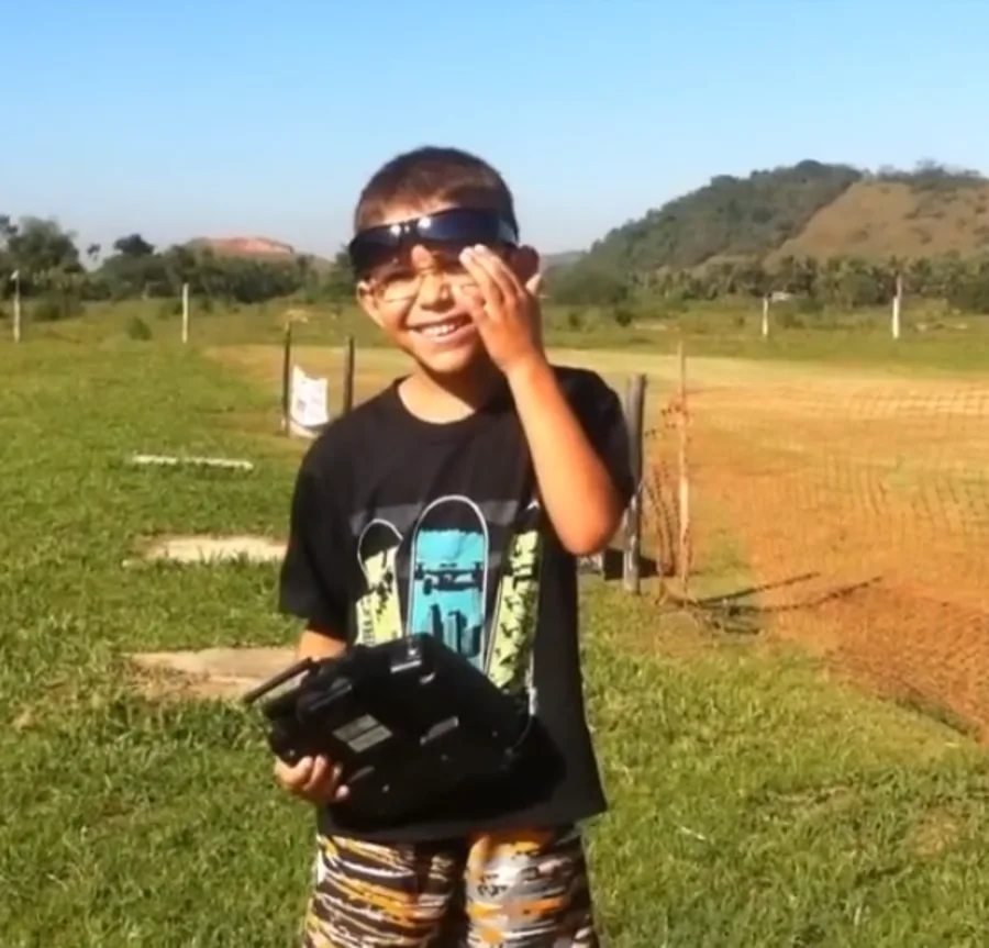 Breno Vilarim criança sorrindo no campo com o rádio controle de aeromodelo